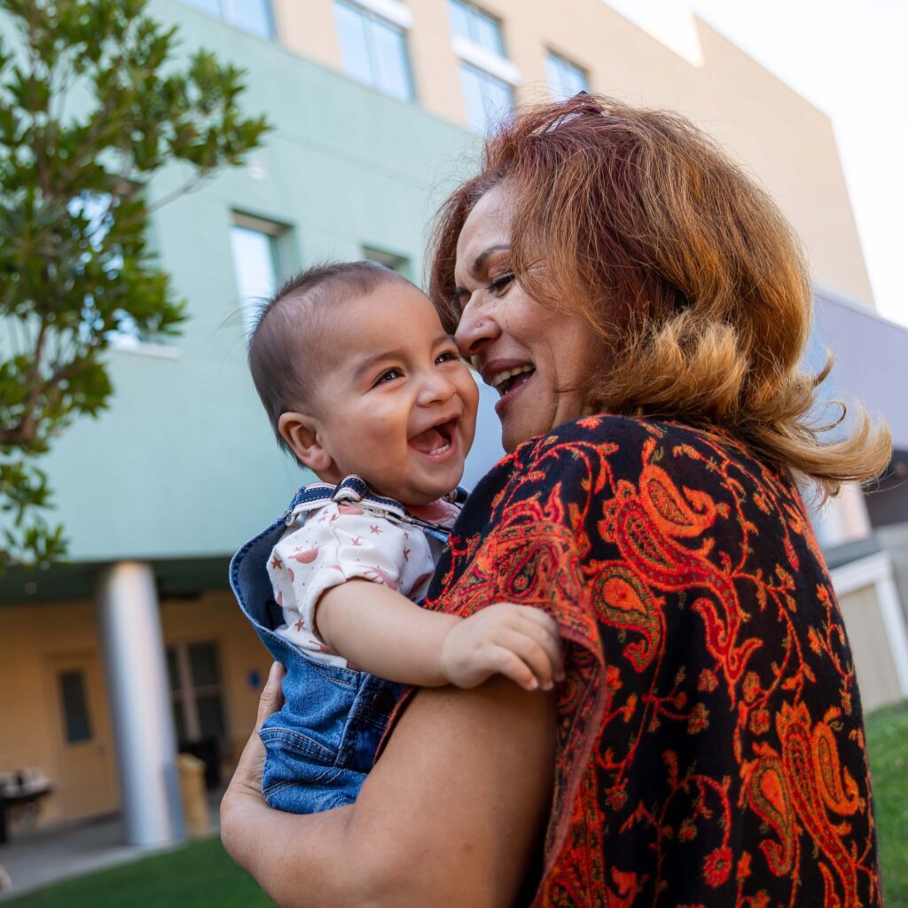 Happy woman holding a laughing baby in front of a building